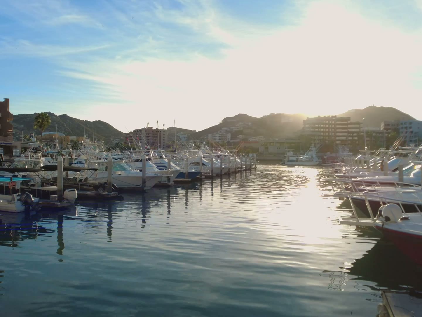 Sunlit yachts stern-to along a harbour wall